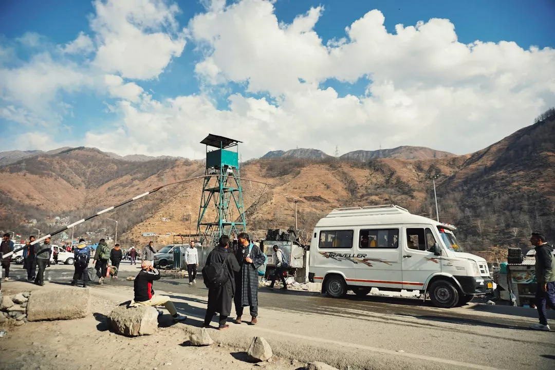 People on a road near a white van and a tall metal tower