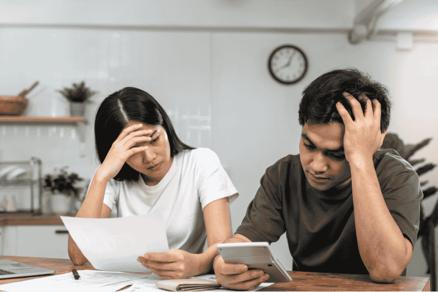 Coppia preoccupata con bollette e smartphone: stress da debiti e rate troppo alte rispetto al reddito disponibile.
