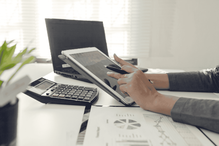 Persona che analizza dati fiscali su tablet con calcolatrice e documenti contabili.