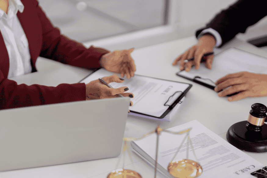 Avvocato e cliente analizzano documenti legali su un tavolo con bilancia della giustizia in primo piano.