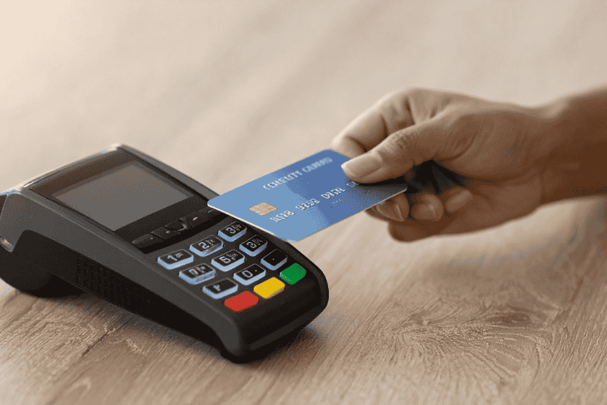 Mano che avvicina una carta di credito blu a un terminale POS per pagamento contactless.