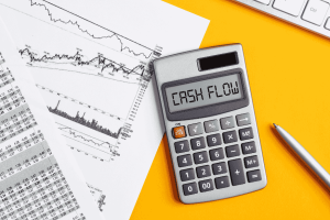 Calcolatrice con la scritta “cash flow” accanto a grafici finanziari su fondo giallo.