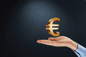 Simbolo dell’euro dorato sospeso sopra una mano su sfondo scuro.