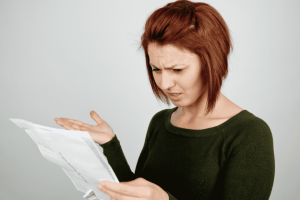 Donna con espressione dubbiosa mentre legge un documento, immagine che mostra il controllo di un estratto conto della carta di credito.