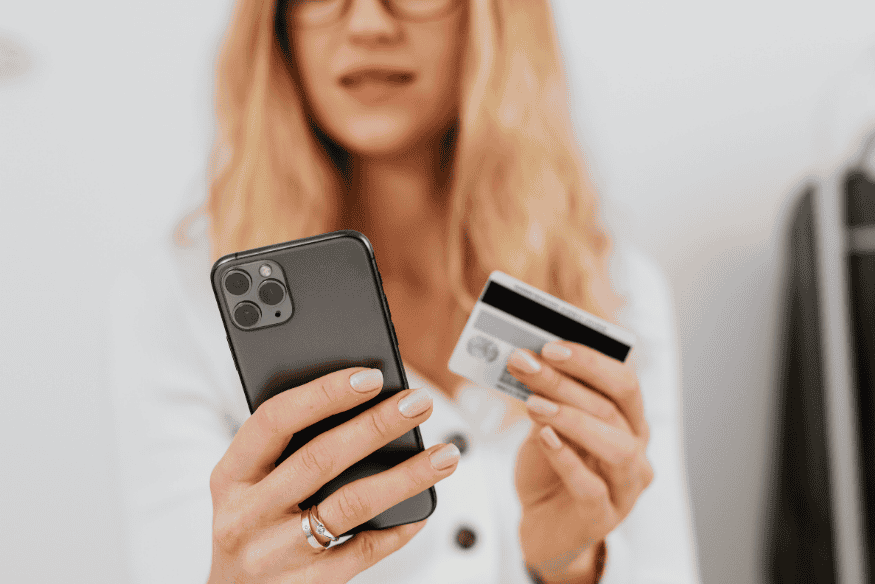 Donna con smartphone e carta di credito in mano mentre gestisce un’operazione online, immagine che illustra come contestare un addebito sulla carta di credito.