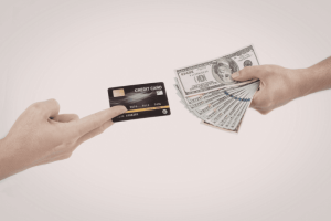 Mano che mostra una carta di credito di fronte a una mano con banconote, immagine che rappresenta rimborso, chargeback e contestazione di un addebito su carta di credito.